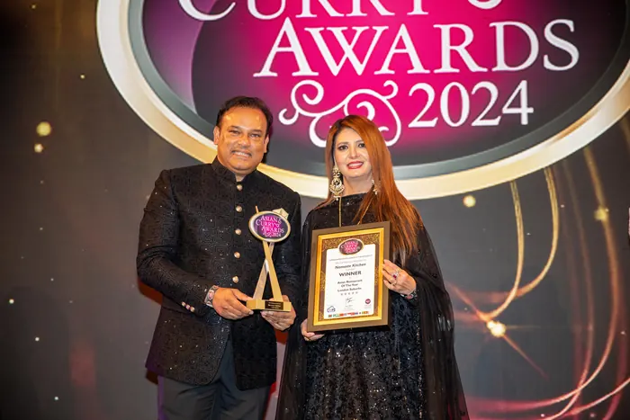 Sabbir Karim on stage with a trophy and framed certificate at the Asian Curry Awards 2024