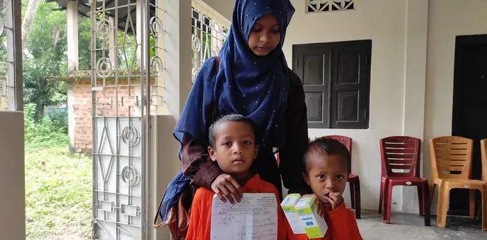 Two young children holding a prescription and a box of medicine with their mother