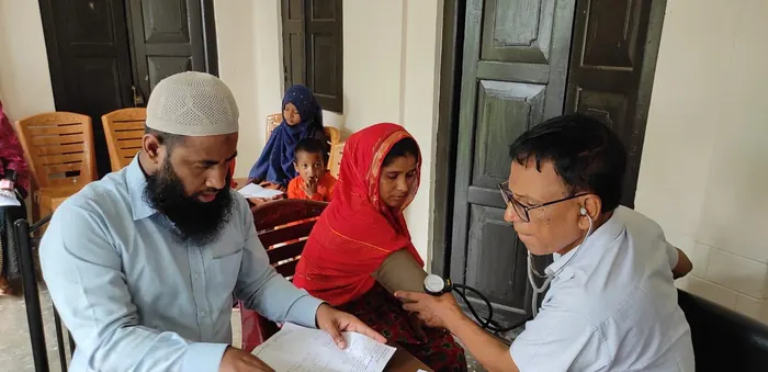 A doctor taking a woman’s blood pressure while a volunteer takes notes