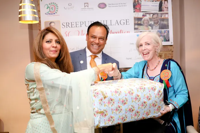 Sabbir Karim with two supporters in front of the Sreepur Village 30 years banner